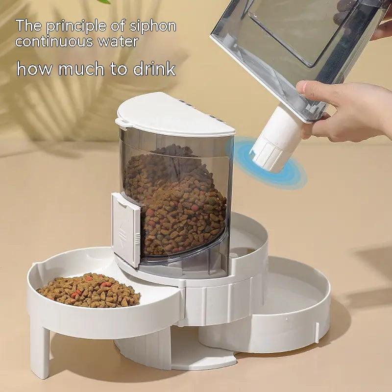 Alimentador automático para mascotas de plástico blanco con dos cuencos y contenedor cilíndrico transparente que sostiene pienso marrón, con base giratoria y compartimento lateral para un dispensado controlado.