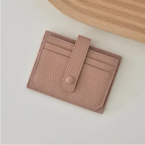 A soft pink ultra thin minimalist textured leather card holder with a matching flap and button closure and strap.