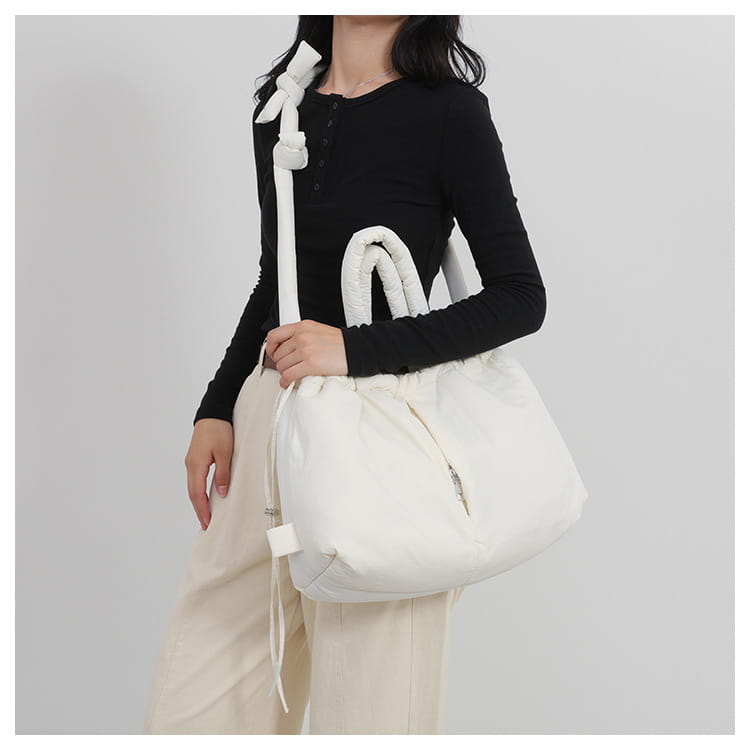 White puffy quilted puffer tote bag made of lightweight nylon with a drawstring knotted strap and zipper closure.