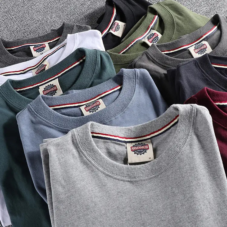 Colección de camisetas tipo jersey de algodón suave de color liso lavado con cuello redondo y manga larga, dobladas con esmero, en gris, azul, verde y negro.