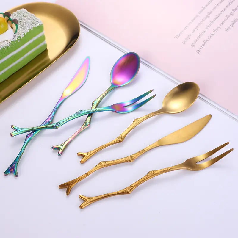 Ensemble d’ustensiles de dessert en acier inoxydable irisés et ton or, avec des poignées semblables à des branches.