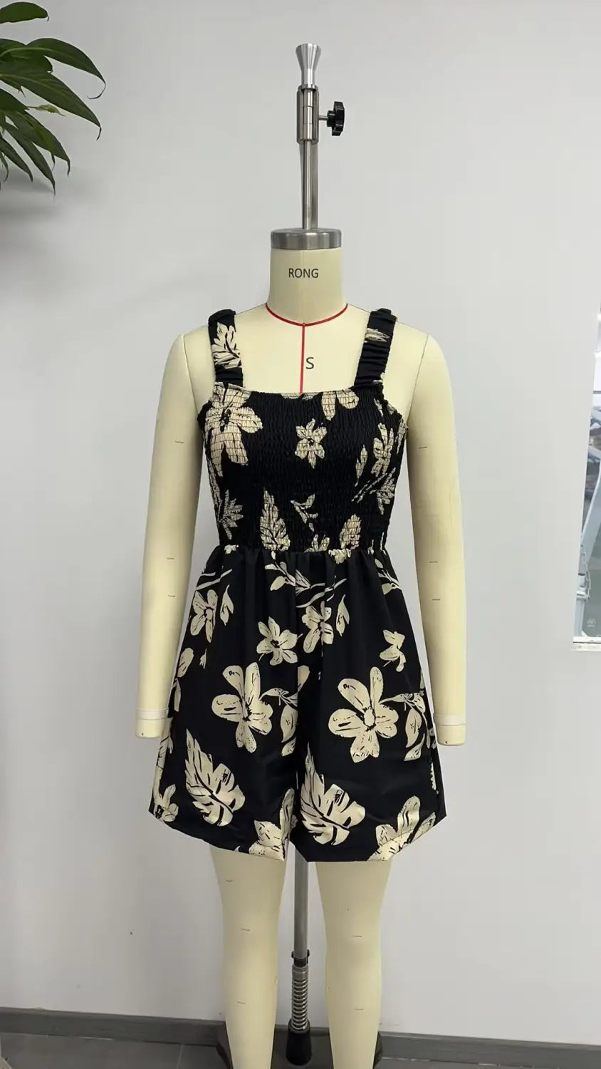 Mono tipo peto con estampado floral negro y patrones botánicos en blanco y tonos crema, con tirantes ajustables y cintura ceñida para vestir en la playa durante el verano.