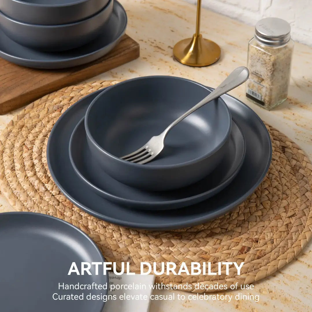 Set of dark gray handcrafted porcelain 12-piece stoneware dinnerware with a matte glaze finish featuring stacked plates and bowls on a woven placemat for service of three.