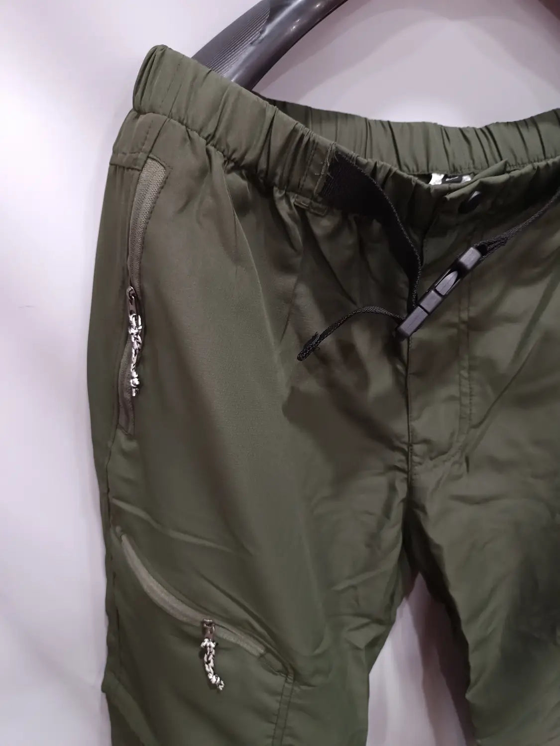 Olive green lightweight convertible tactical hiking pants with elastic waistband and silver zipper accents designed for outdoor use.