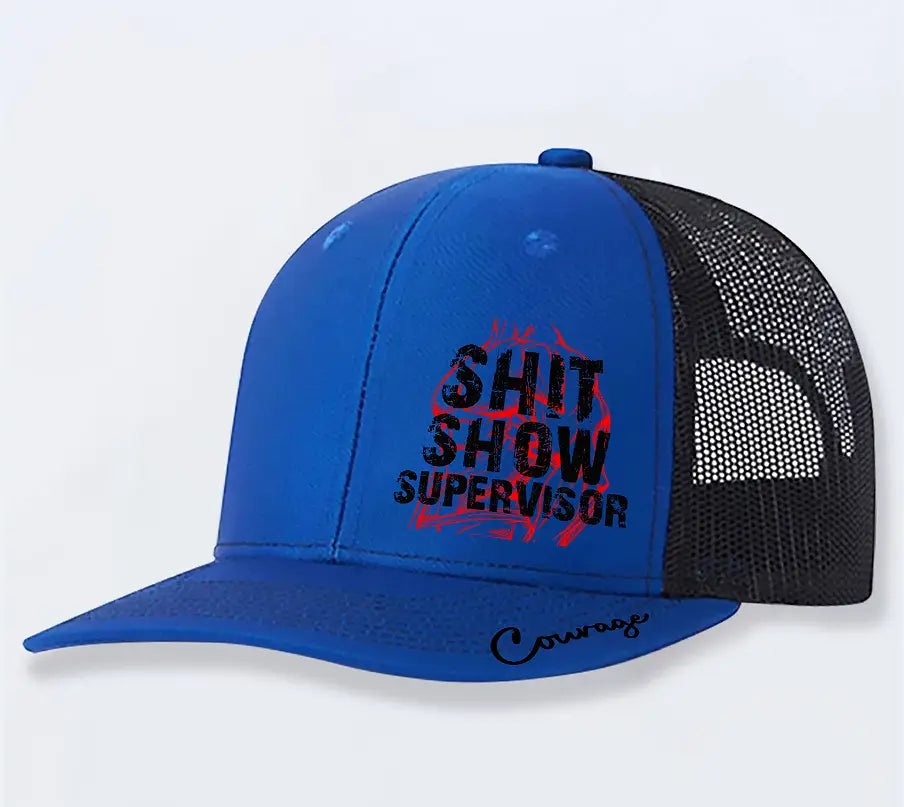 Blue trucker hat with black mesh back and bold shit show supervisor graphic in black and red on the front featuring a cursive courage logo embroidered near the brim for men.