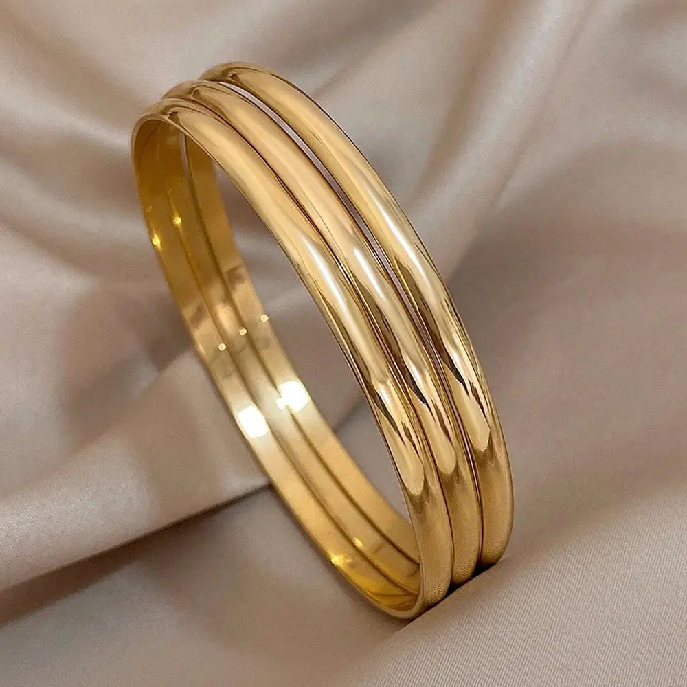 Three sleek polished gold 18k gold plated minimalist stackable bangles stacked together.
