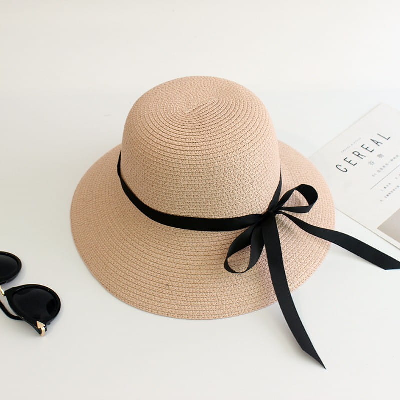 Wide brim straw sun hat in beige woven straw featuring a black satin ribbon bow around the crown.