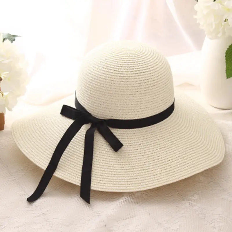 Off-white wide brim straw sun hat with a black satin ribbon bow around the crown.