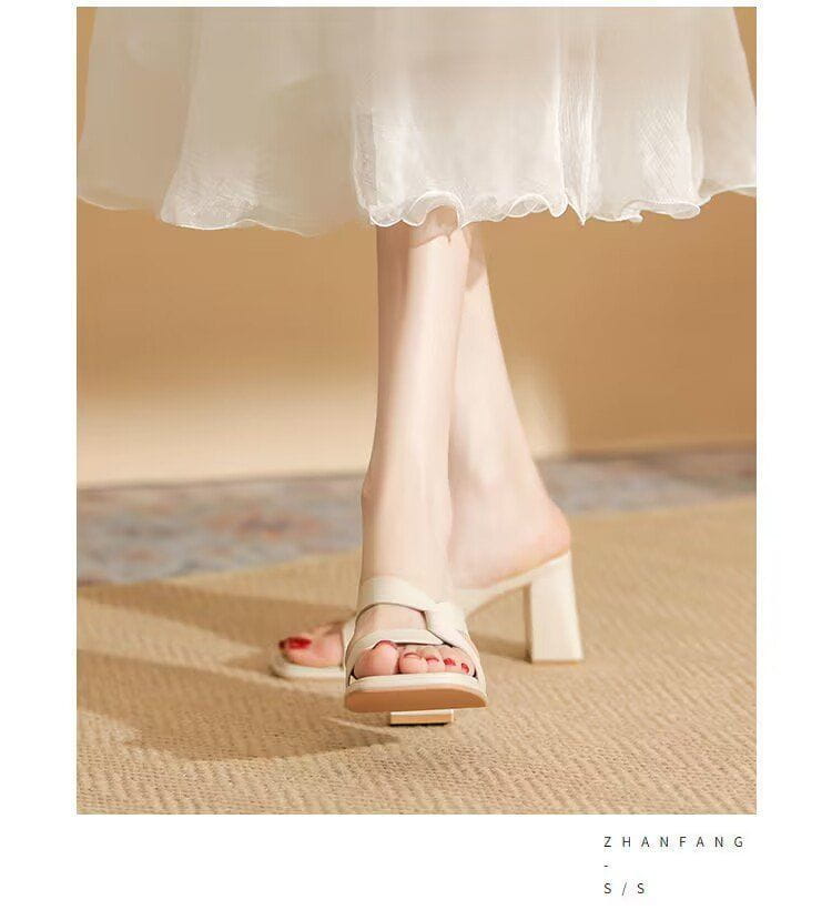 Cream-colored leather chunky heel open toe sandals featuring a block heel and minimalist crisscross strap design.