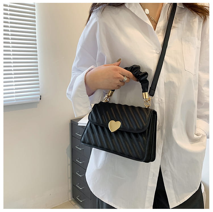 Black quilted crossbody handbag with a gold heart-shaped clasp and a ruched fabric handle.