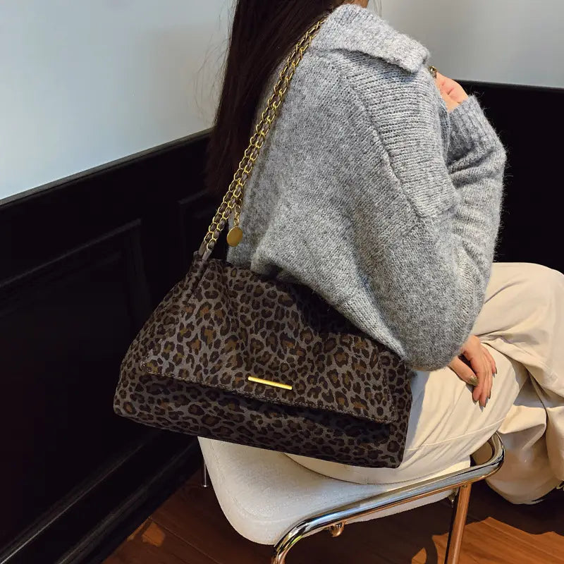 A leopard print crossbody bag featuring a gold chain strap and a matching metallic clasp.