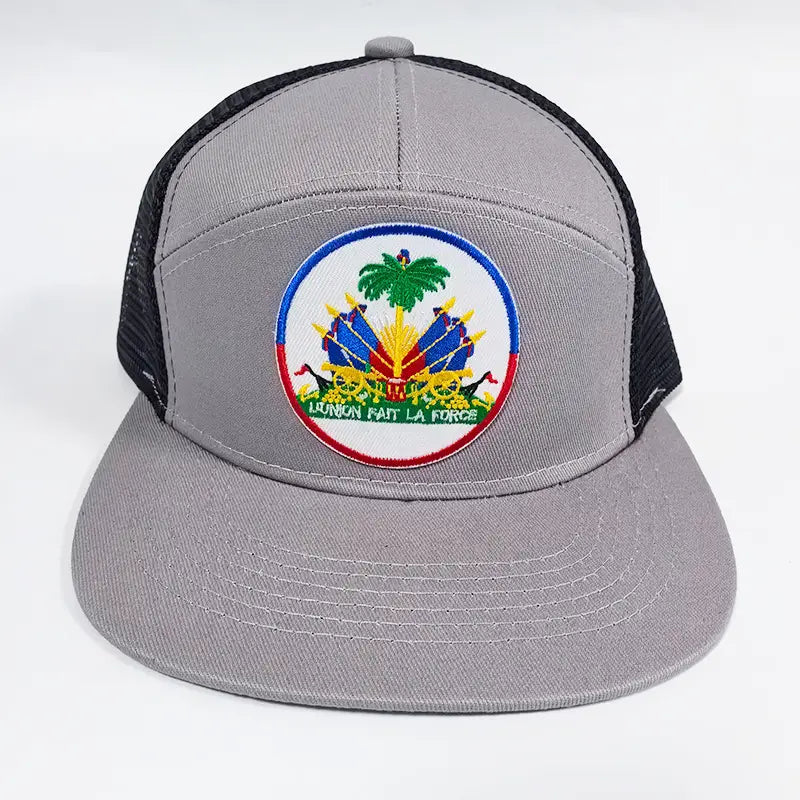 gray trucker hat with black mesh back featuring a circular embroidered patch of the Haitian national emblem with palm trees cannons and the motto union fait la force in green lettering designed for sun protection in cream blue tones