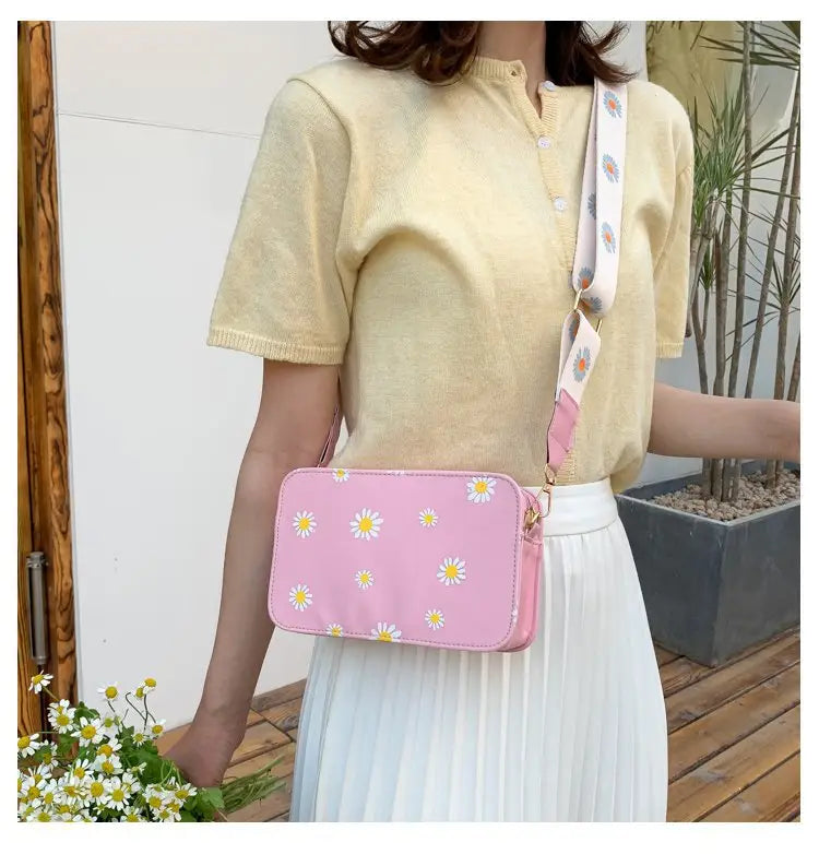 Pink crossbody bag made of pu leather with white daisy print and pink chain strap suitable for casual use.