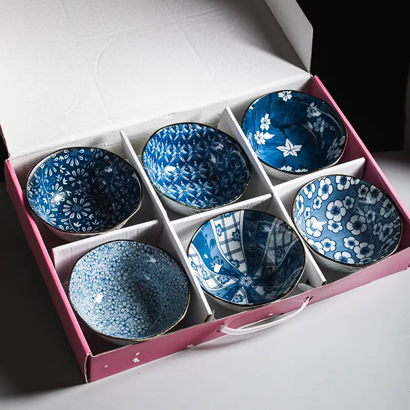 Set of six blue and white ceramic bowls with intricate floral and geometric patterns and gold rim, made of porcelain, neatly arranged in a pink gift box.