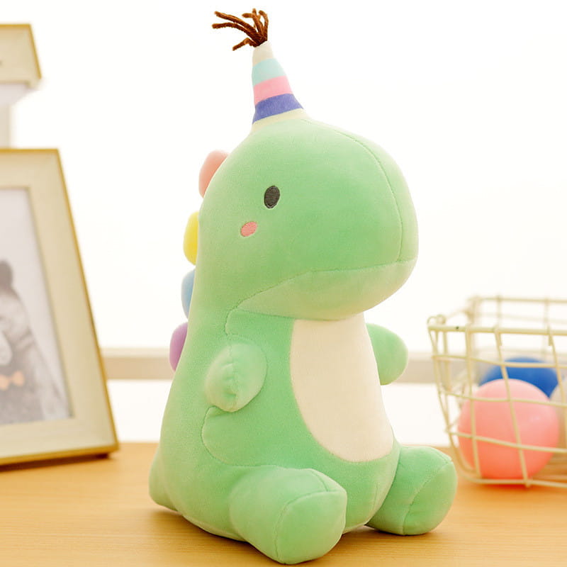 Ein weiches grünfarbenes Dinosaurier-Plüschtier aus Kuscheltiermaterial mit einer farbenfrohen, gestreiften Party-Kappe mit braunem Fransenbesatz.