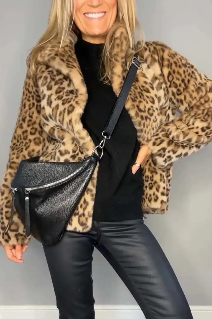 Schwarze, strukturierte Ledertasche im Crossbody-Stil mit silberfarbenem Reißverschluss und Ketten-/Tassel-Detail, das den Mantel aus Kunstfell mit Leopardenmuster und Kapuze ergänzt.