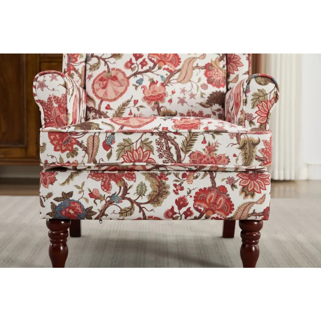 Una mullida silla tipo ala con respaldo capitoné floral, tapizada en un tejido vibrante con flores rosadas rojas y verdes llamativas sobre un tejido color crema, con patas de madera retro.