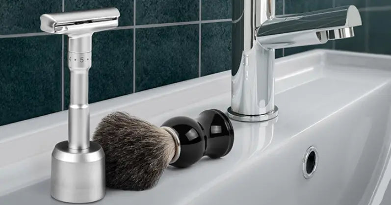 Silver safety razor with sleek modern design and adjustable blade settings displayed alongside badger hair shaving brush with black ceramic handle for enhanced grooming.