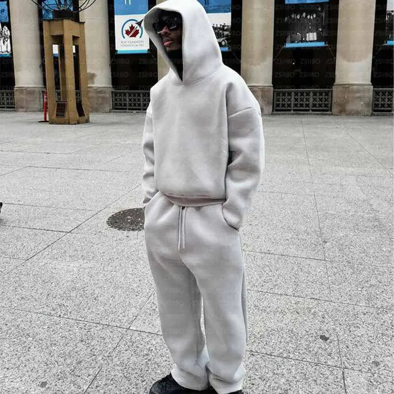 Une personne portant un ensemble oversize unisexe streetwear gris clair, comprenant un sweat à capuche et un pantalon de survêtement assorti avec cordon.