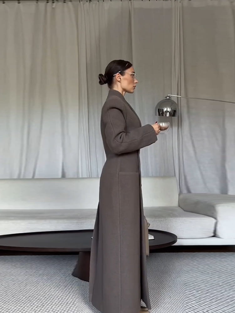 A charcoal gray wool coat for women featuring a sleek waisted long silhouette with a structured design and large front pockets.