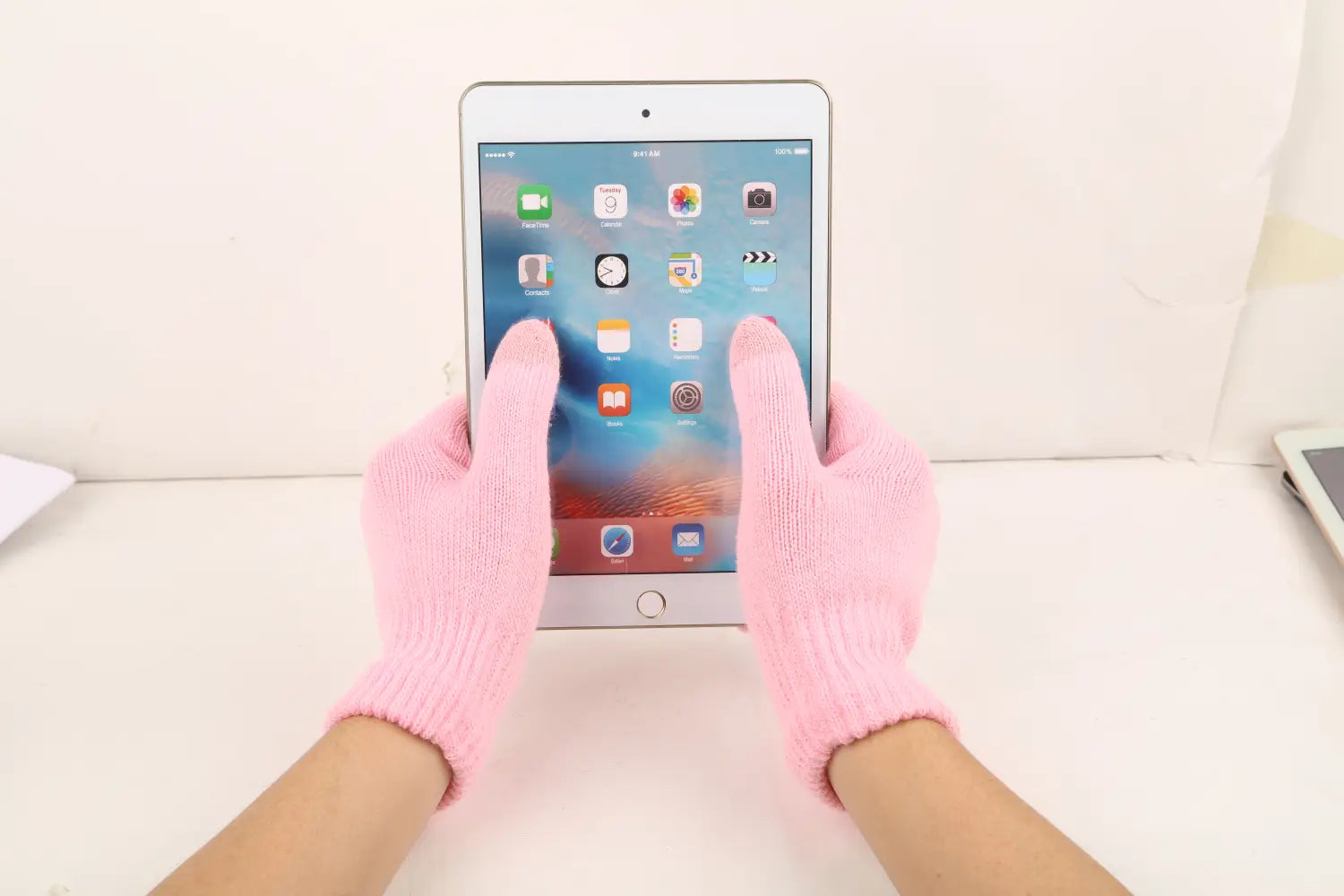 Hände, die rosafarbene, gestrickte Touchscreen-Winterstrickhandschuhe tragen, halten ein weißes iPad mini mit silbernem Rahmen und Home-Button und demonstrieren eine warme unisex Nutzung.