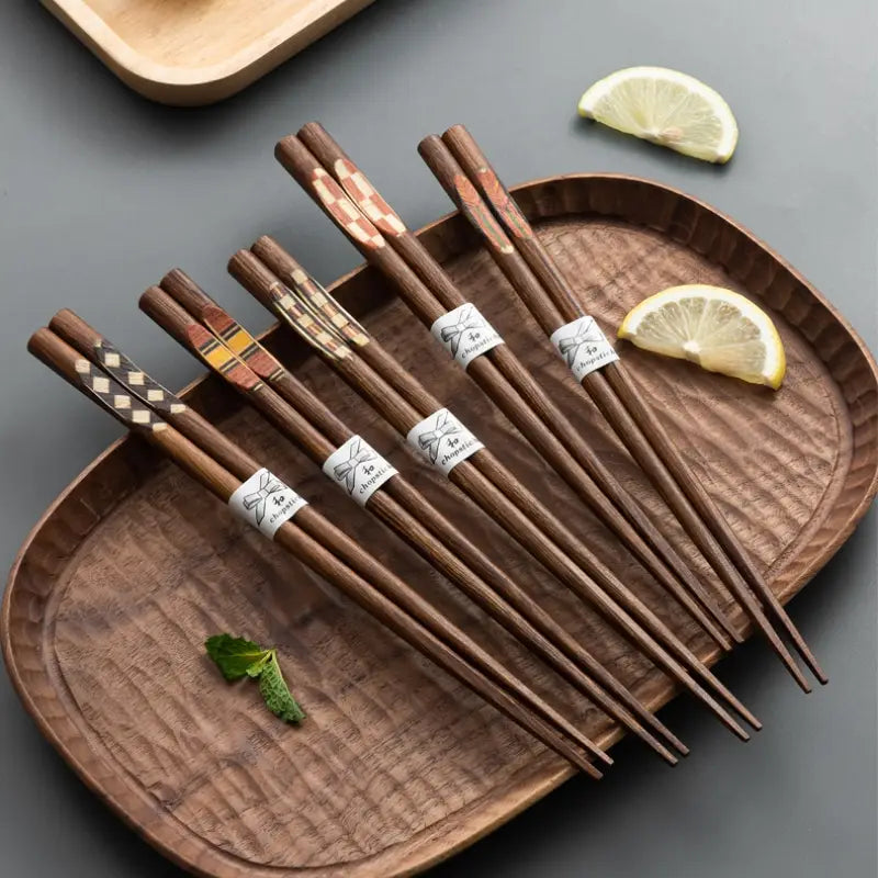 Set of six wooden chopsticks with decorative inlaid patterns and white paper bands arranged on a textured brown serving tray from a wooden chopsticks set with non slip tips 10 pairs.