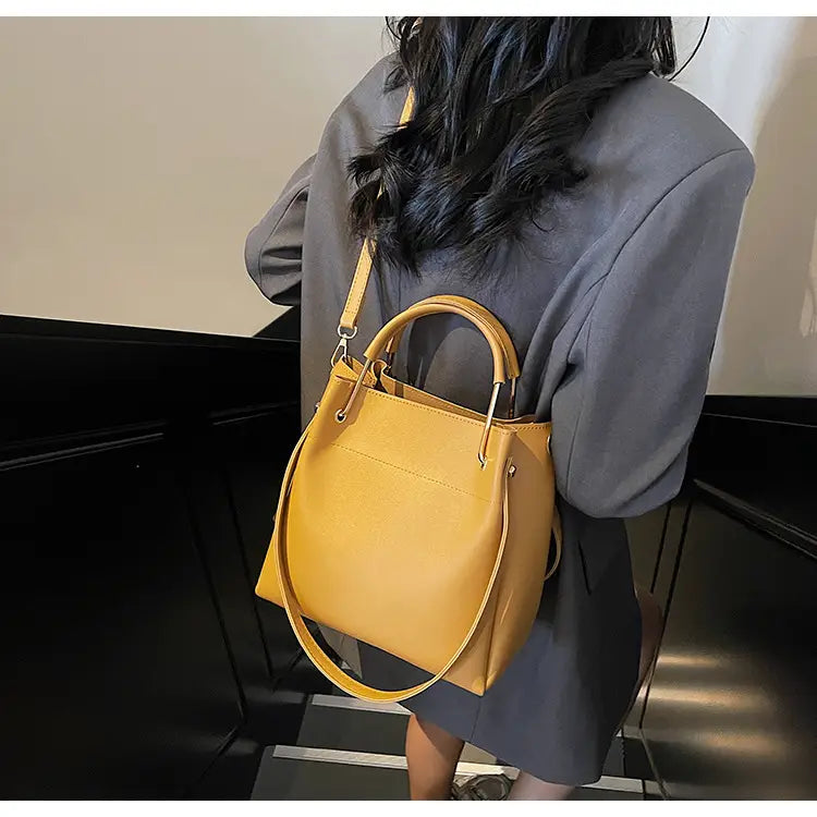 A mustard-yellow minimalist leather bucket bag with top handles and a detachable shoulder strap.