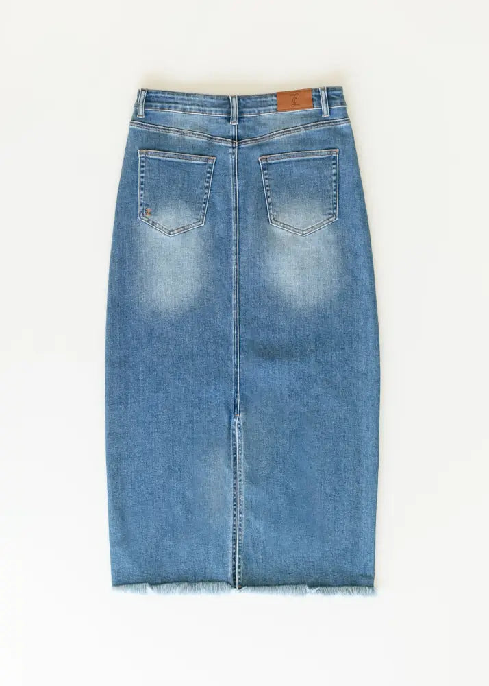 Back view of dakotah raw hem high waisted denim maxi skirt in medium blue wash with two back pockets and frayed hem