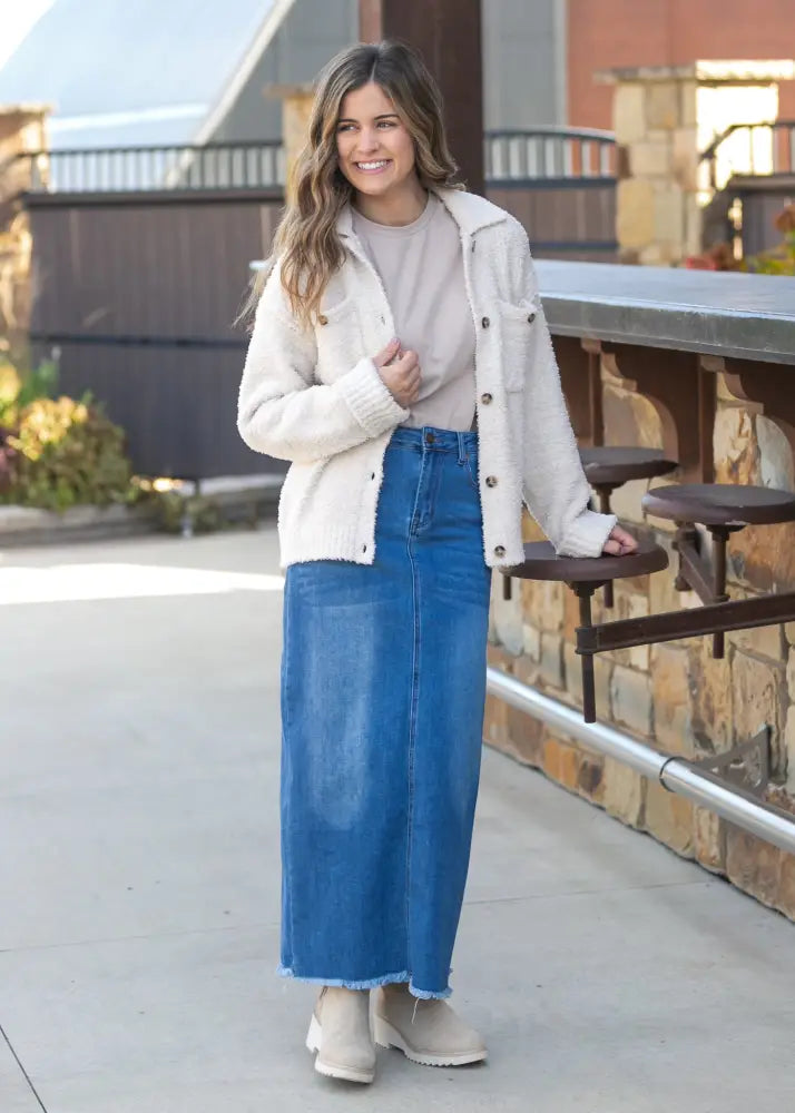 A woman wears a cream shearling jacket over a beige top paired with a dakotah raw hem high waisted denim maxi skirt