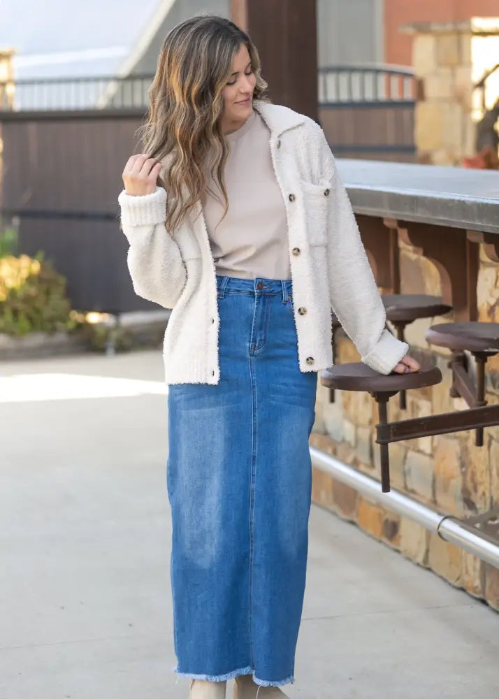 Cream-colored shearling jacket with button closures and a cozy textured exterior paired with a denim maxi skirt
