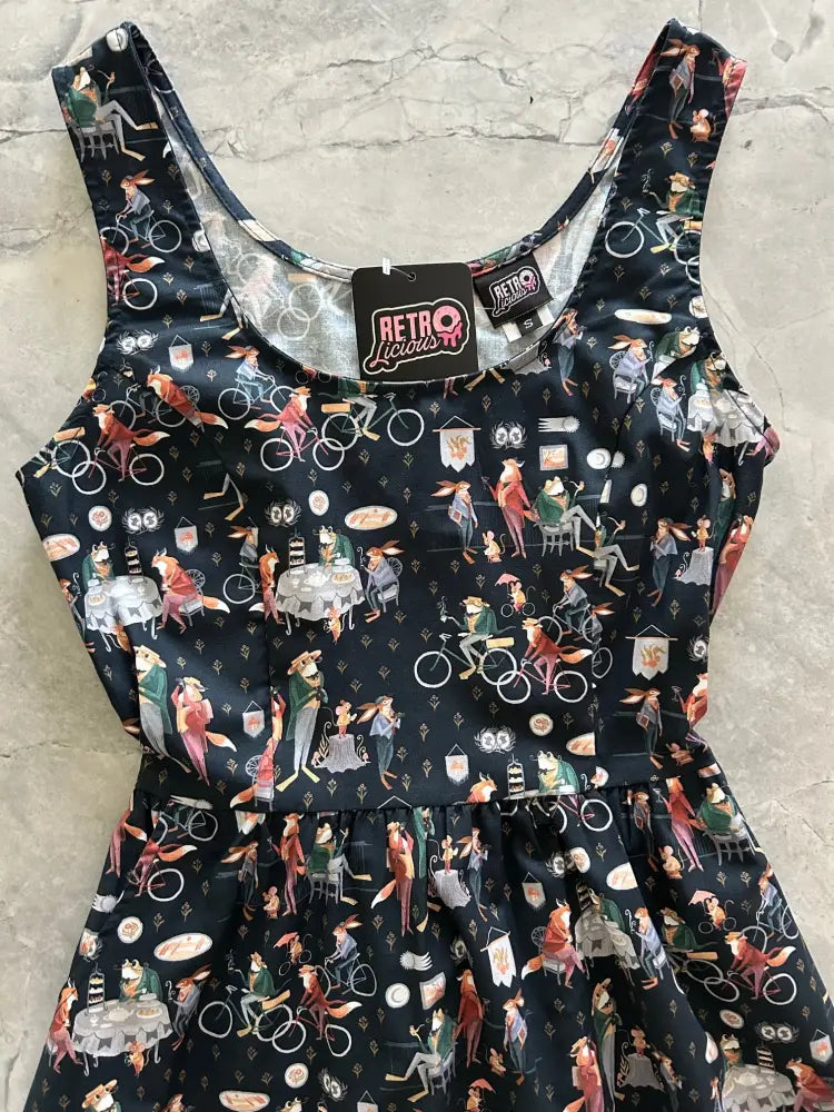 Black sleeveless fit and flare dress with dapper fox print featuring whimsical characters on bicycles and cafes with pockets