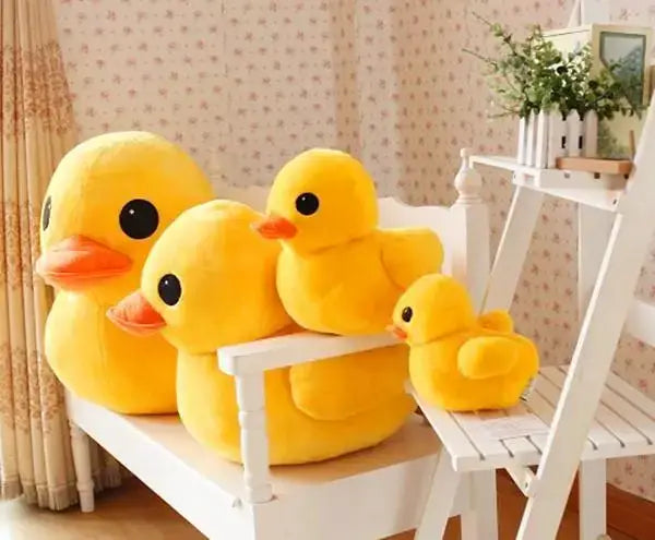 Set einer Familie aus flauschigen gelben Gummienten-Weichstofftieren mit orangen Schnäbeln und schwarzen Augen, weich gepolsterte Stofftiere, angeordnet auf einer weißen Holzbank.