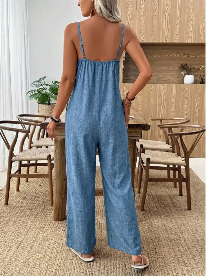 細いストラップとリラックスしたフィット感のブルーデニムのジャンプスーツを着用した女性。ウィメンズ向けリネンのワイドレッグジャンプスーツとしてスタイリングされています。