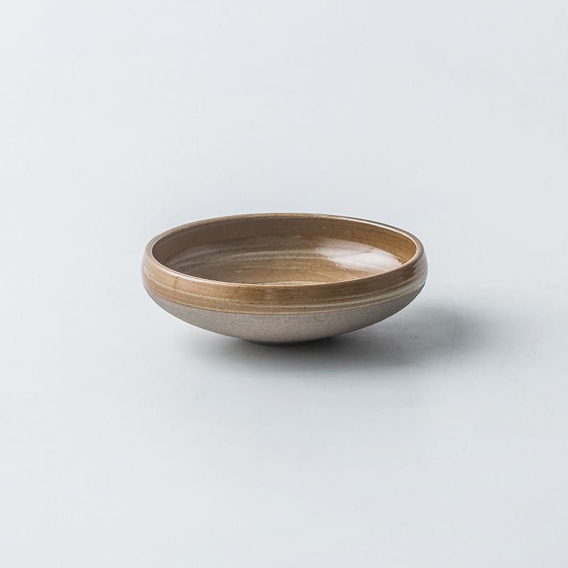 A minimalist ceramic bowl from a ceramic tableware set retro Japanese dinnerware featuring a matte beige exterior, glossy tan interior, and subtle concentric ridges along its rim.