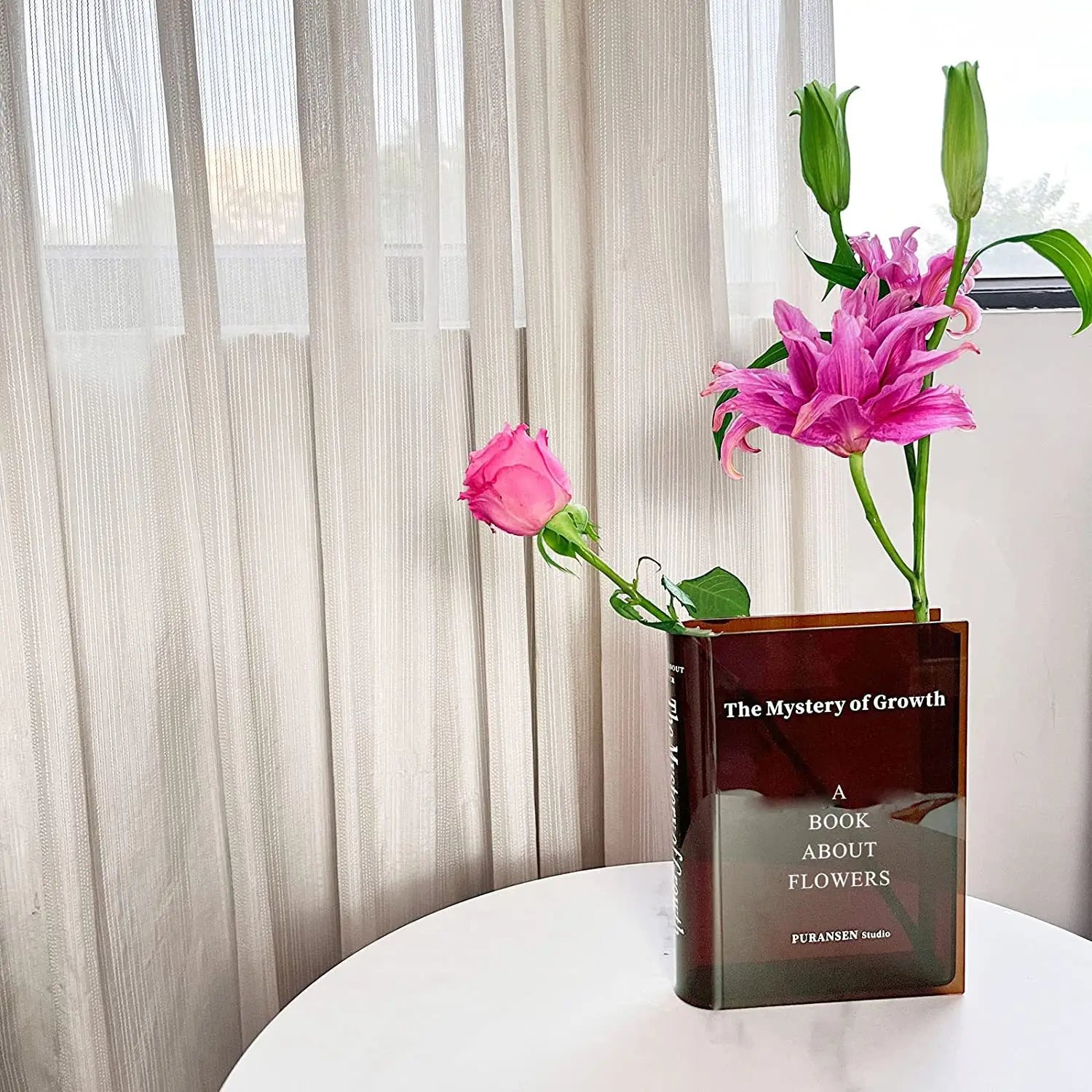 jarrón de flores de libro de acrílico en ámbar translúcido con forma de libro que sostiene lirios rosados vibrantes y una rosa para decoración moderna del hogar.