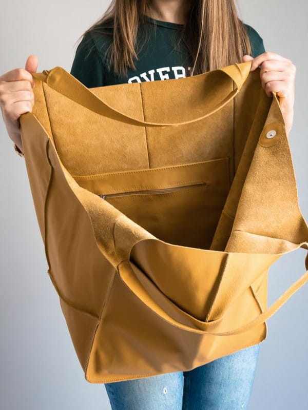 A tan suede leather tote bag with a spacious interior featuring multiple compartments and a zipper pocket designed as a large capacity soft slouchy shoulder bag.