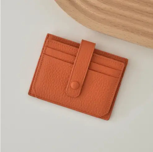 A compact orange textured leather ultra thin minimalist card holder with a flap closure secured by a single button and a strap.