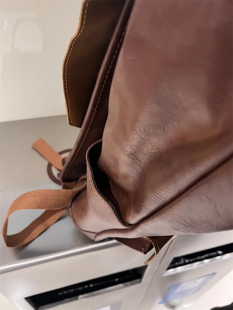 Vintage leather college backpack in brown with visible stitching and fabric strap designed for large capacity travel use.