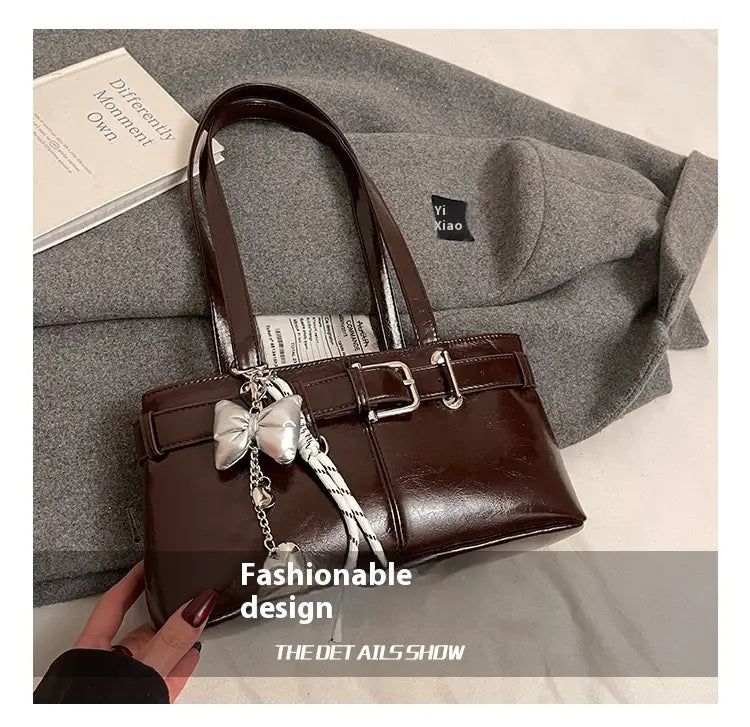 Brown faux leather shoulder bag with silver buckle and decorative bow charm.