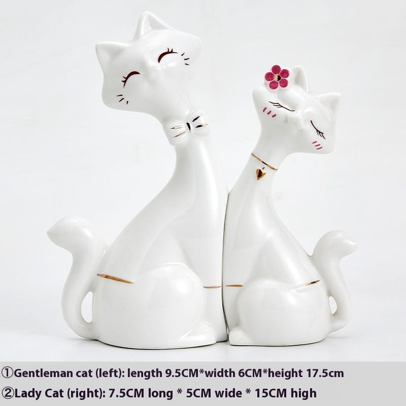 White ceramic cat figurines with modern gold accents featuring one with a pink flower and the other with a bow tie for home decor.