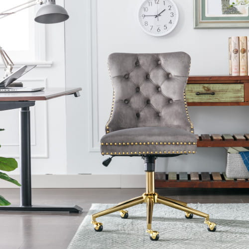 Chaise de bureau en velours capitonné gris avec piètement pivotant en métal à finition ton sur ton or et garniture à clous décoratifs, conçue pour un siège d’espace de travail élégant.
