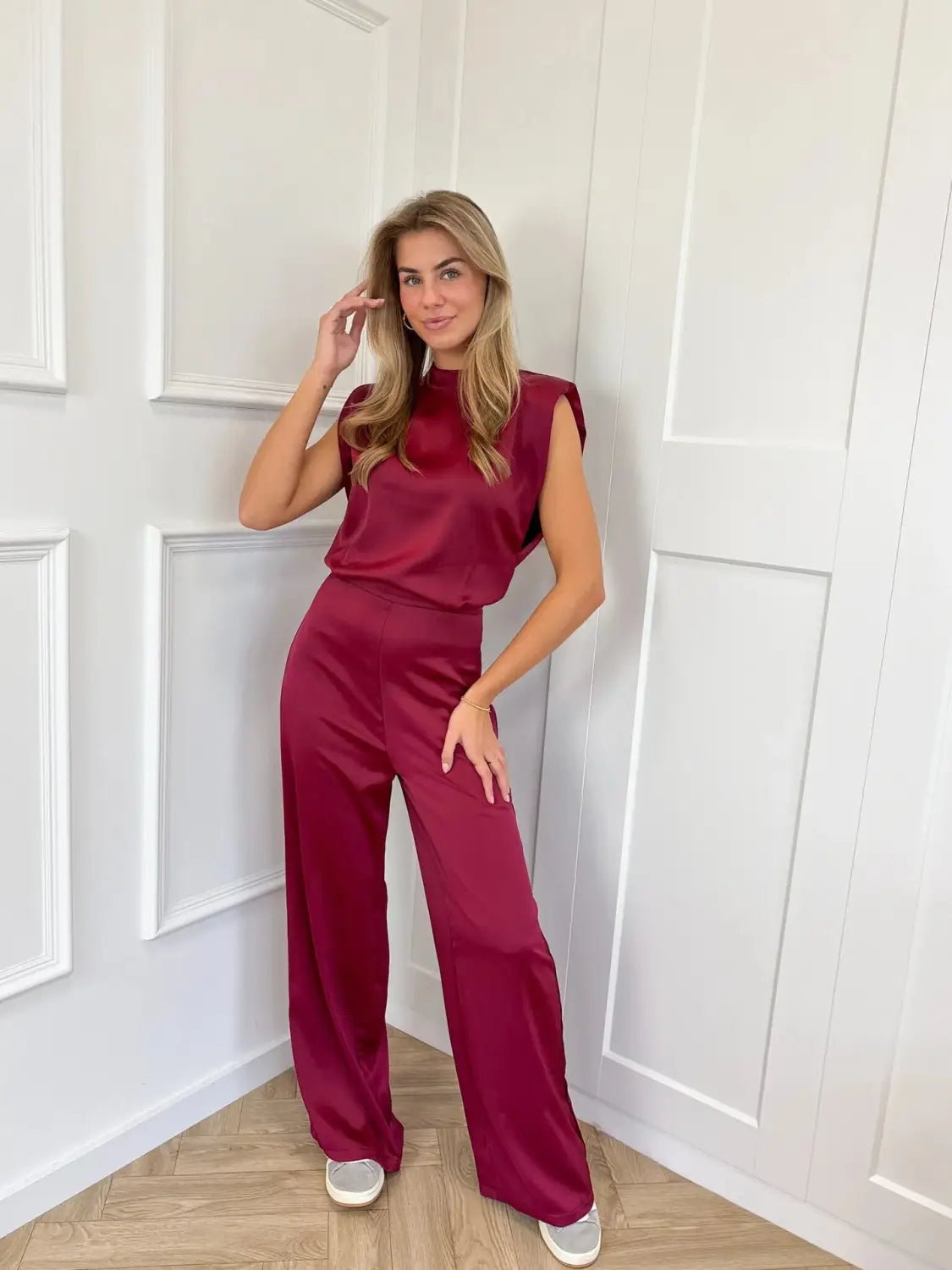 A woman wearing a sleek sleeveless burgundy satin backless evening dress jumpsuit with straight wide-leg pants.
