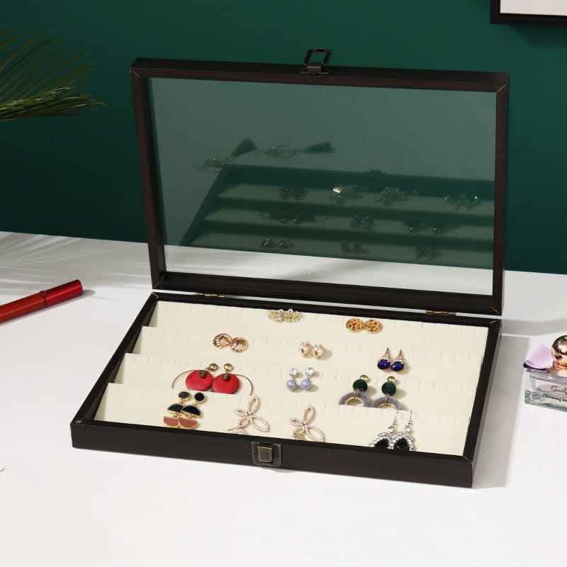 Rosewood jewelry display box with glass lid featuring black rectangular design and white interior compartments holding various earrings.