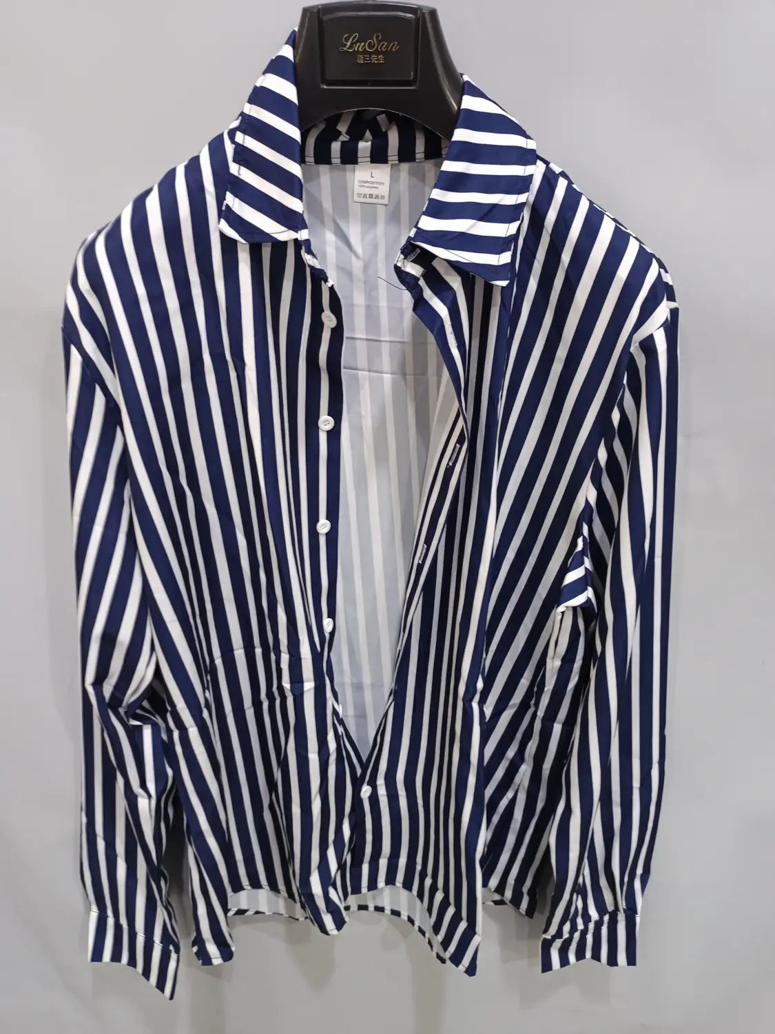 Chemise décontractée à manches longues rayée verticalement bleu marine et blanc pour hommes, avec col classique, suspendue sur un cintre noir.