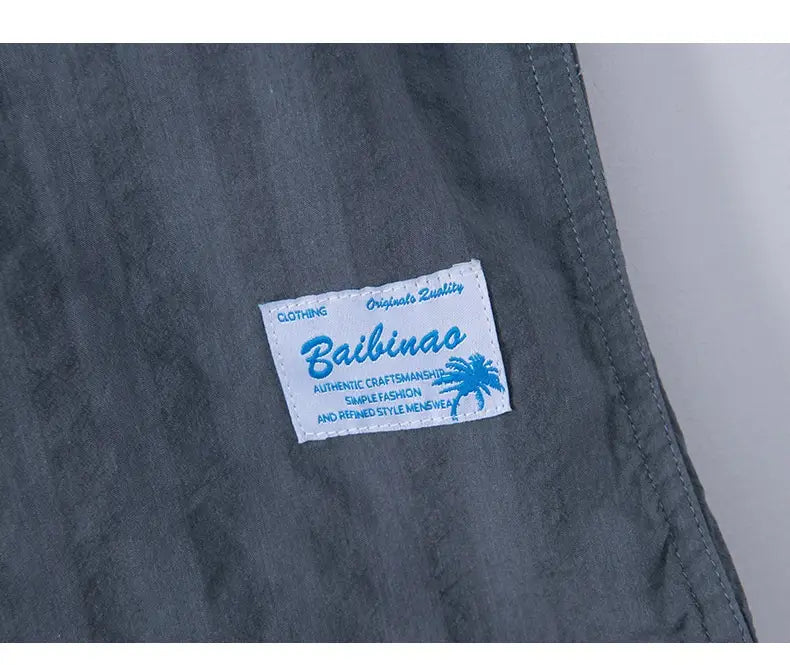 Kurzärmliges Baumwollhemd im lässigen Stil aus dunkelgrau gestreiftem Stoff, mit einem weißen Label mit blauem Text und einem Palme-Motiv, gebrandet als bailiniao.