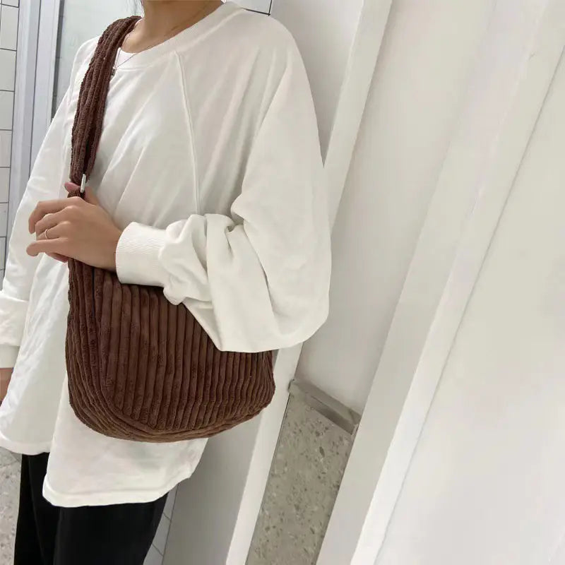 Brown corduroy crossbody shoulder bag with textured ribbed fabric and a simple slouchy design featuring an adjustable strap.