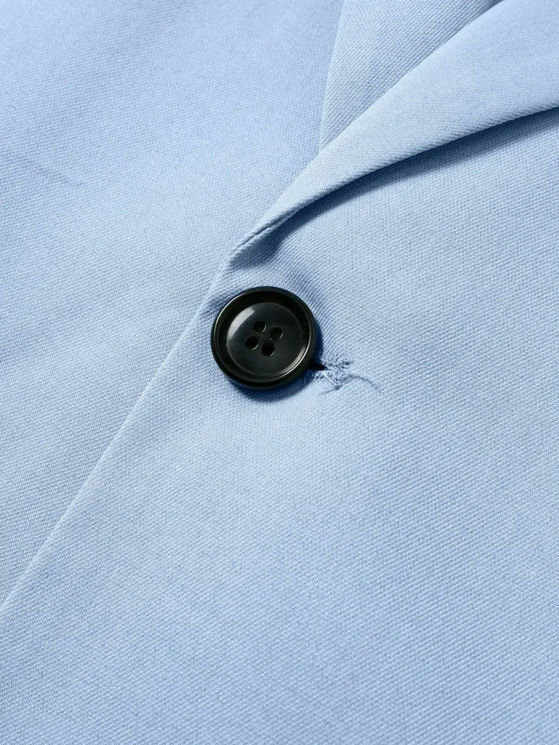 a black four-hole button sewn onto light blue fabric of a light blue short sleeve suit and shorts set