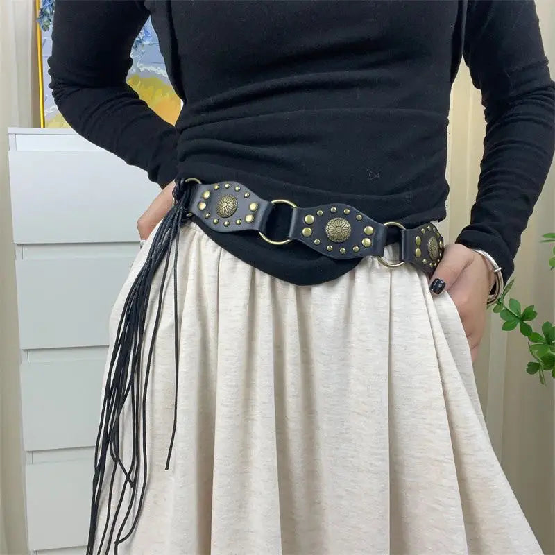 Schwarzer Gothic-Punk-Lederharness-Gurt mit messingfarbenen, kreisförmigen Nieten, Metallringen und schwarzem Quastenfransenbesatz.