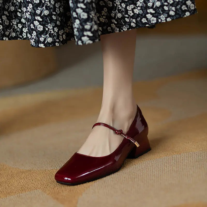 Burgundy patent leather mary jane flats with square toe and low block heels shown from the back side.