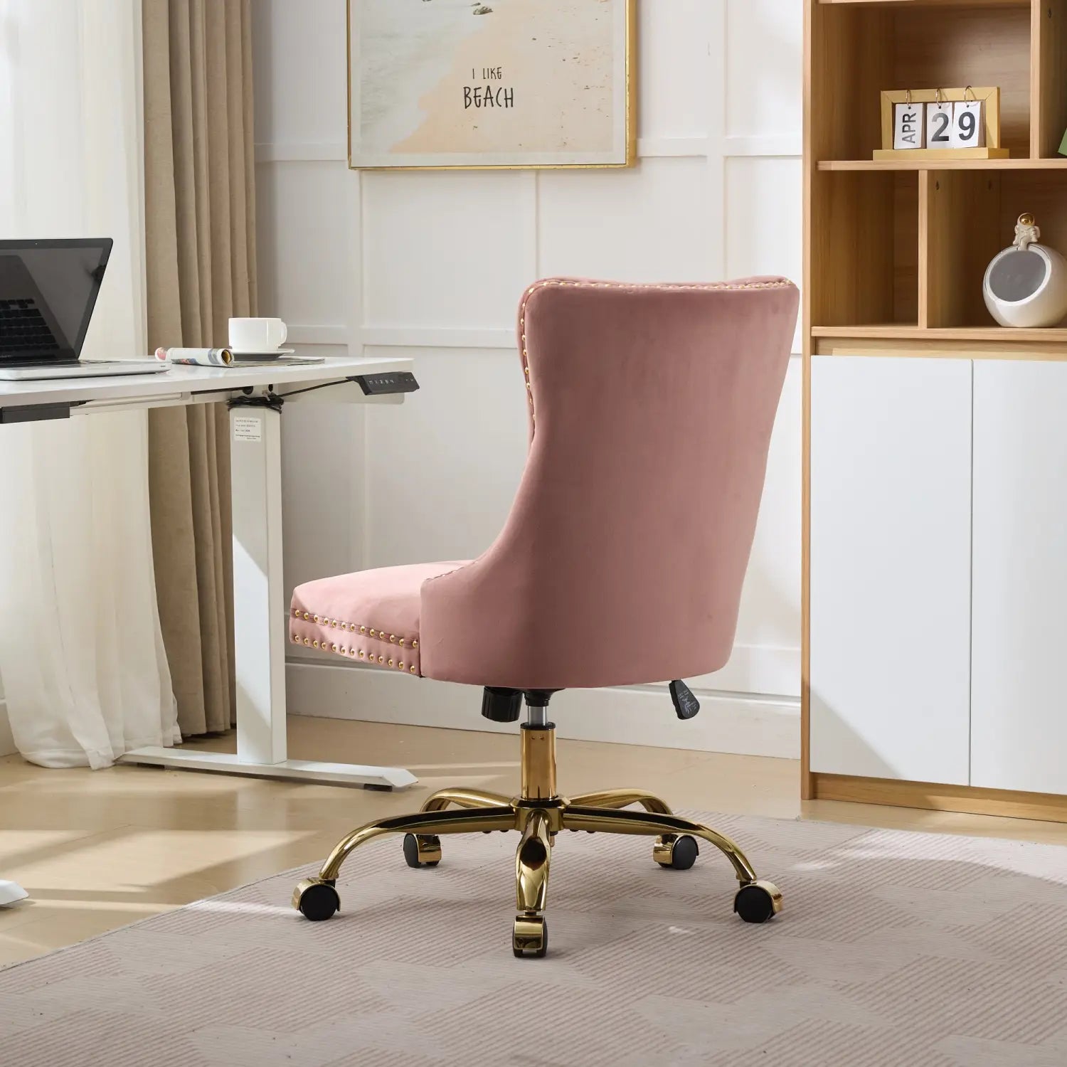 Fauteuil de bureau en velours rose poudré, capitonné, comportant une base en métal ton doré et une bordure à clous décoratifs, conçu pour un espace de travail.